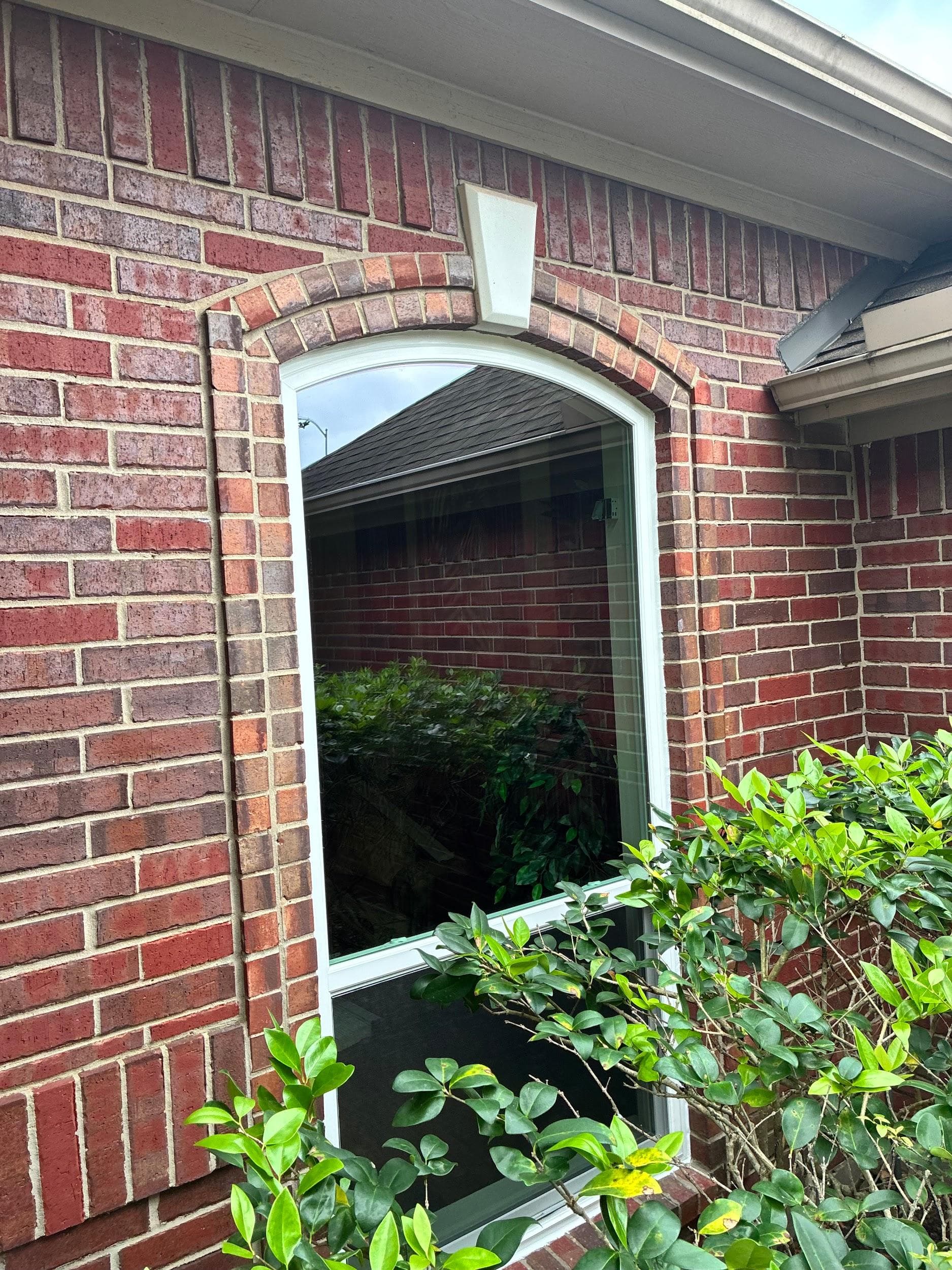 White single-hung window set into an arched brick opening on a red-brick home