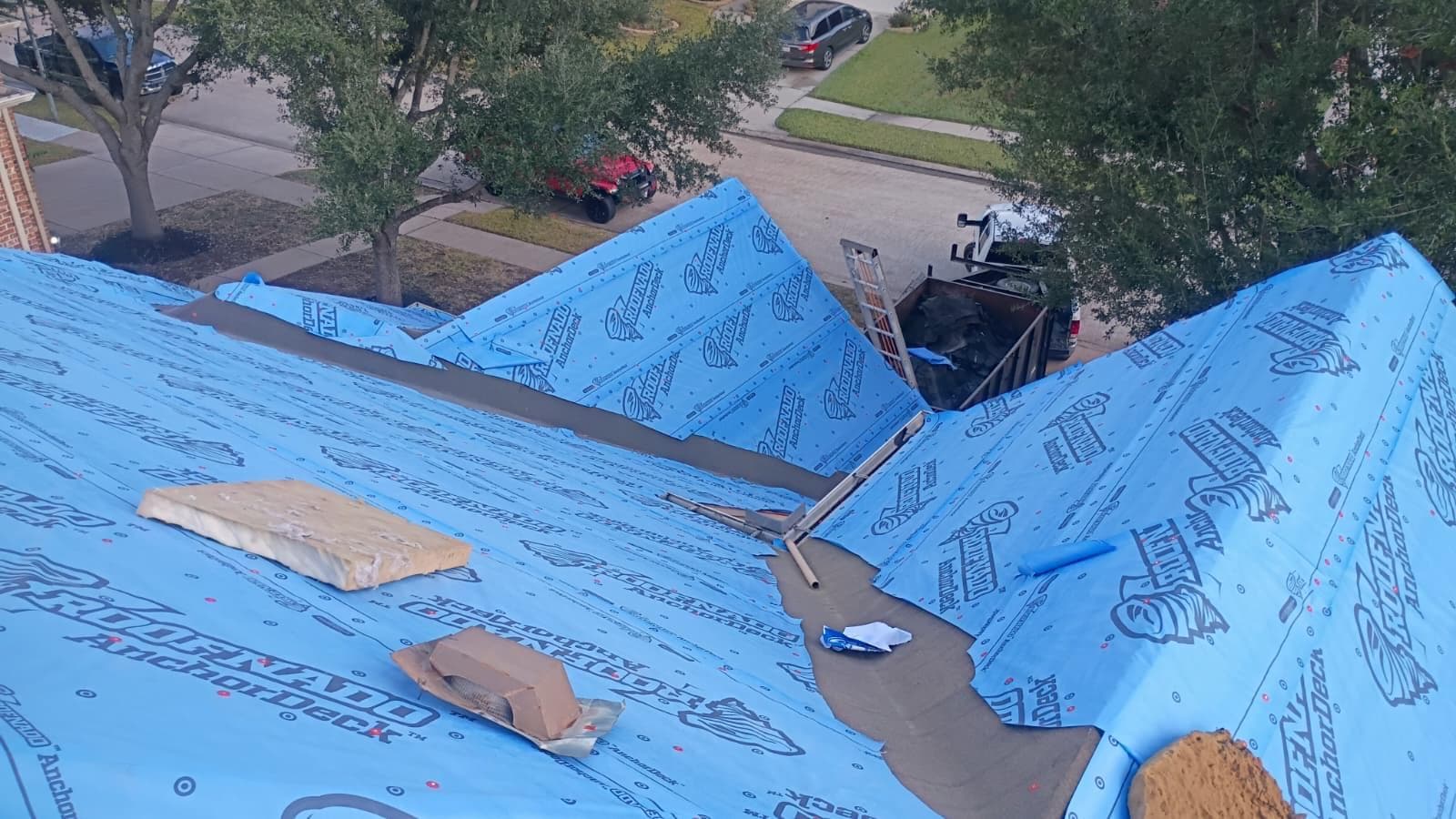 Storm-damaged Houston roof dried in with synthetic underlayment, debris trailer at the curb