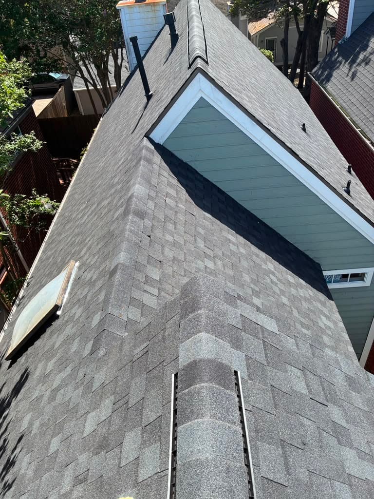 Finished charcoal shingle roof wrapping around a gable dormer with skylight