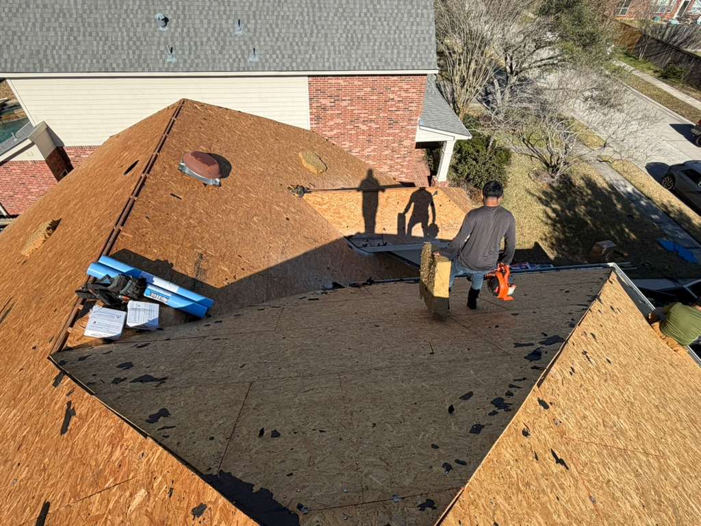 Roofer carrying decking across a re-decked roof on a two-story brick home