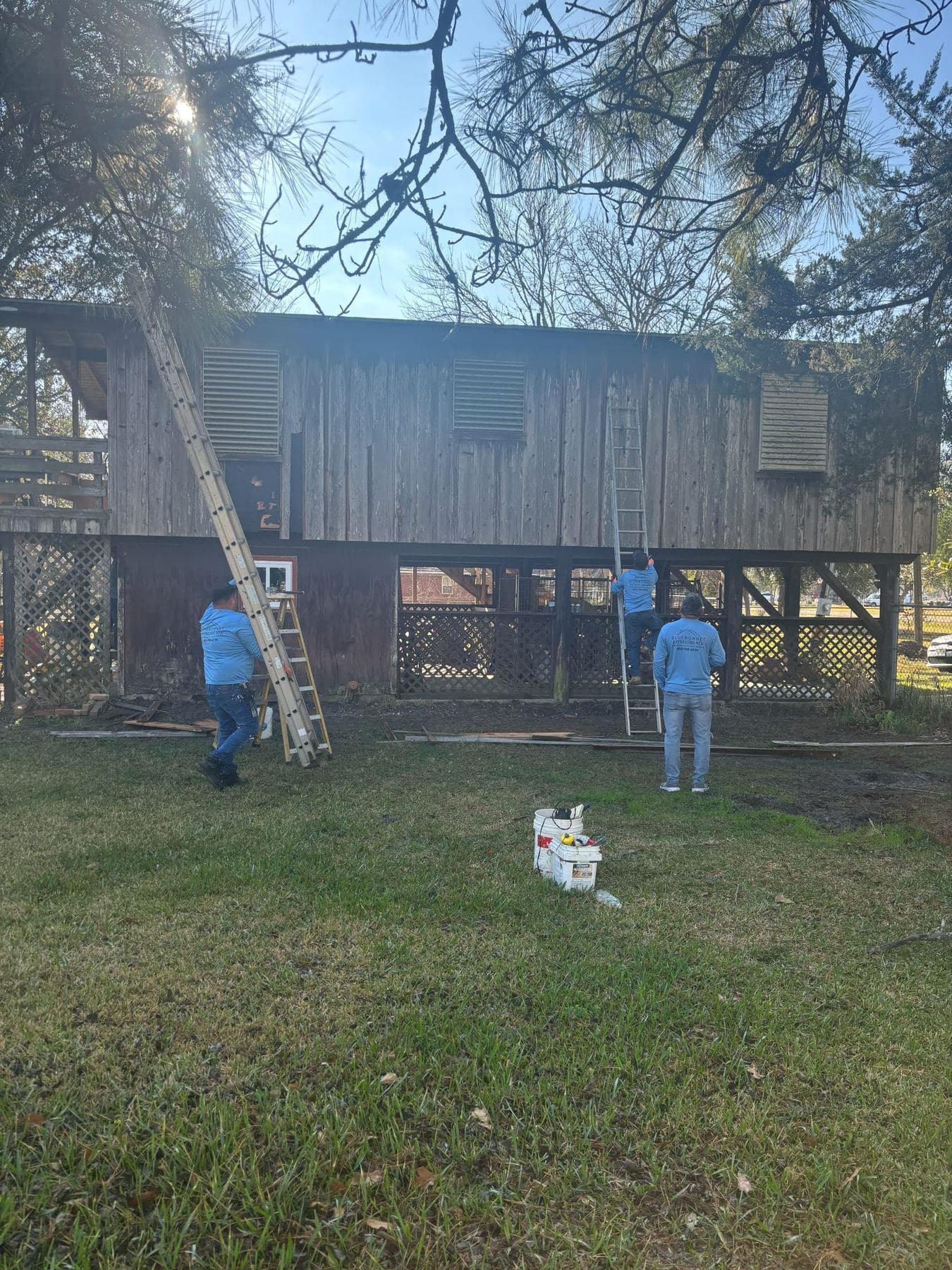 Bluebonnet crew on ladders prepping the stilted house for new siding